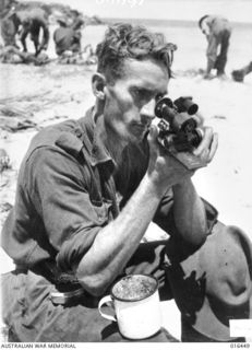 NEW GUINEA. 14 JANUARY 1944. PRIVATE R.E. MAVIN OF WYONG, N.S.W. LOOKING AT A JAPANESE ARTILLERY DIAL-SIGHT WHICH WAS FOUND AMONG THE MACHINE GUN PARTS THROWN IN THE SEA BY THE JAPANESE NEAR THE ..