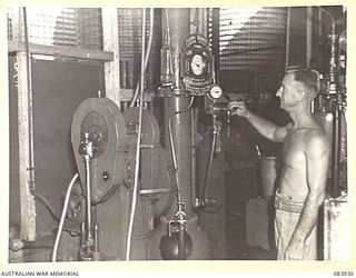 LAE, NEW GUINEA. 1944-12-12. LIEUTENANT C.J. MULLENS, OFFICER COMMANDING A SOFT DRINK FACTORY FOR ARMY CANTEENS SERVICE WITHIN LAE BASE SUB-AREA, ADJUSTS AN AUTOMATIC CARBONATER MACHINE WHICH PUMPS ..