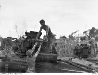 BOUGAINVILLE. 1945-03-30. CORPORAL B.A. DENNE (1) AND TROOPER W.R. YOUNG (2), OF 2/4 ARMOURED REGIMENT, UNLOADING THREE INCH AMMUNITION FROM A MATILDA TANK FOR DRYING AFTER THE INTERIOR WAS FLOODED ..