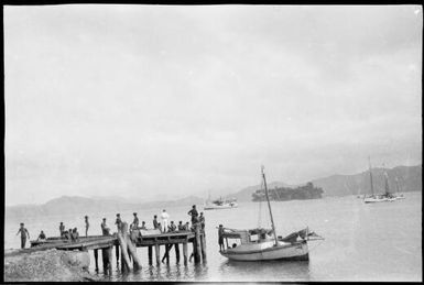 People on jetty with moored boats and a tree covered island in background, New Guinea, ca. 1929 / Sarah Chinnery