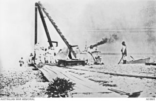 A German landing party from the Nurnberg standing beside a crane and rail equipment on Fanning Island. The island was the site of a central Pacific telephone cable relay station. The party cut ..