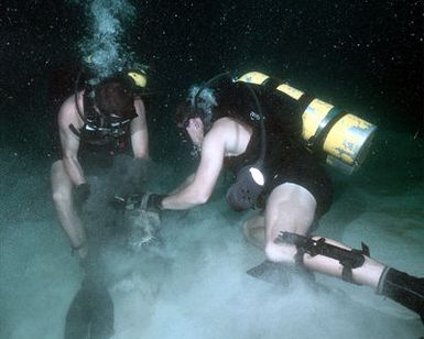 Aviation Ordinanceman First Class (AO1) Jonathan A. Hamm, Explosive Ordnance Disposal Mobile Unit Five (EODMU5), Detachment Marianas and CHIEF Parachute Rigger (CPR) Frank V. Marrs, prepare to lift old sunken ammo cans with 20mm rounds to the surface. The ammo is being salvaged from a barge, which sunk after WWII