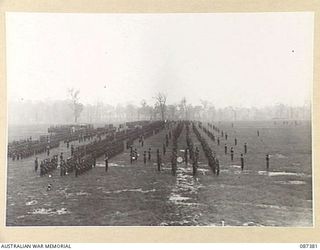 HERBERTON, QUEENSLAND. 1945-03-03. 24 INFANTRY BRIGADE TROOPS PRESENT ARMS AS MAJOR GENERAL G.F. WOOTTEN, GENERAL OFFICER COMMANDING 9 DIVISION ARRIVES DURING HEAVY RAIN FOR THE PRESENTATION OF ..