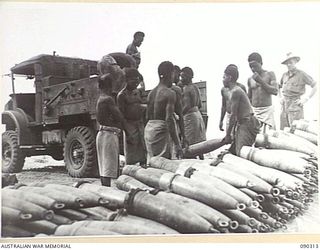 PURIATA RIVER AREA, BOUGAINVILLE. 1945-04-03. NATIVES OF ANGAU, ATTACHED 7 INFANTRY BRIGADE, LOADING 155 MM SHELLS ONTO A TRUCK FOR TRANSPORT TO AN AMMUNITION DUMP AFTER UNLOADING FROM A BARGE AT ..