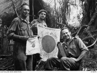 1943-09-14. NEW GUINEA. KOMIATUM RIDGE. CPL. CHARLES LETTERS, OF SYDNEY AND CPL. FRANK YOUNG, OF PORT MORESBY, DISPLAY A JAPANESE FLAG FOUND ON KOMIATUM RIDGE AFTER THE ENEMY HAD BEEN FORCED FROM ..