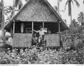 LUNGGA, GUADALCANAL, SOLOMON ISLANDS, 1944-02-29. LIEUTENANT COMMANDER D.S. MACFARLANE, DEPUTY SUPERVISING INTELLIGENCE OFFICER (DSIO), NAVAL INTELLIGENCE DIVISION, RAN, STANDING WITH TWO NATIVE ..