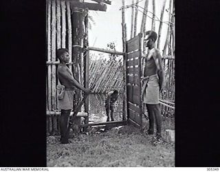 SEGI, NEW GEORGIA. BRITISH SOLOMON ISLANDS PROTECTORATE. C.1944. GUARDED BY NATIVE POLICE, A JAPANESE PRISONER OF WAR TAKES A BATH IN THE STOCKADE. (NAVAL HISTORICAL COLLECTION)