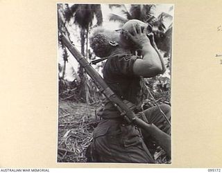 COCONUT KNOLL, KIARIVU, NEW GUINEA, 1945-08-11. PRIVATE I.E. JONES, 2/7 INFANTRY BATTALION, QUENCHING HIS THIRST FROM A COCONUT, BEFORE THE LONG HIKE DOWN THE KNOLL TO WATER. THE UNIT IS ..