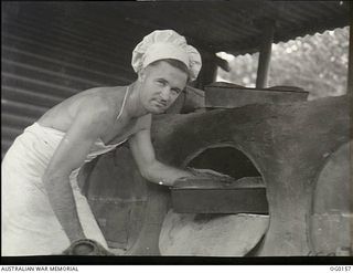 VIVIGANI, GOODENOUGH ISLAND, PAPUA NEW GUINEA. C. 1943-07. 13205 LEADING AIRCRAFTMAN A. H. HALL OF MOOROOPNA, VIC, BAKER OF NO. 7 MOBILE WORKS SQUADRON RAAF, AT THE OVEN BAKING THE DAILY BREAD FOR ..