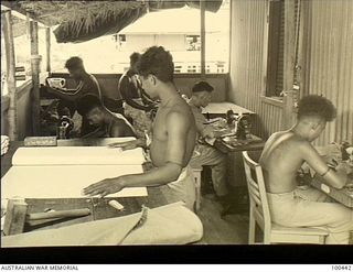 Ela Beach, New Guinea. 1944-05-10. Archie Pon-Tung, Chinese tailor, operating a treadle sewing machine (second right), and supervising his native staff making household linen on the verandah of the ..