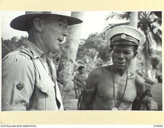 BASAMA, NEW GUINEA. 1944-07-13. WARRANT OFFICER II, K. WOODMAN, AUSTRALIAN NEW GUINEA ADMINISTRATIVE UNIT, INTERVIEWING KING BUMBU, HEREDITARY CHIEF OF THE HUON GULF NATIVES. KING BUMBU WAS ..