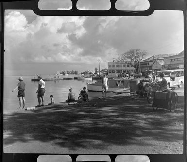 Papeete waterfront, Tahiti, showing locals fishing and flying boat in the distance
