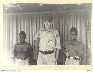 LAE, NEW GUINEA. 1944-10-18. NGX350 MAJOR E.W. JENYNS, DEPUTY ASSISTANT DIRECTOR OF NATIVE LABOUR AND OFFICER IN CHARGE, LAE BASE SUB AREA, AUSTRALIAN NEW GUINEA ADMINISTRATIVE UNIT AND TWO OF HIS ..