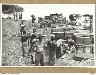 WALINGAI BEACH, NEW GUINEA. 1944-01-04. NATIVES BRINGING SUPPLIES ASHORE FROM BARGES TO THE STORES DUMP OF THE 27TH PLATOON, 2/6TH SUPPLY DEPOT COMPANY. IDENTIFIED PERSONNEL ARE: NX8504 STAFF ..