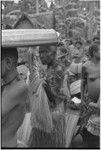 Mortuary ceremony, Omarakana: mourning woman, her face blackened with ash and head shaved, holds up fiber skirt valuable