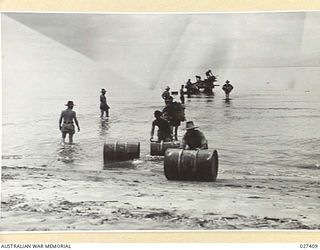 WANIGELA, NEW GUINEA. 1942-10. SAPPERS OF 2/4TH FIELD COMPANY, ROYAL AUSTRALIAN ENGINEERS, UNLOADING STORES AND EQUIPMENT FROM A LARGE NATIVE CANOE