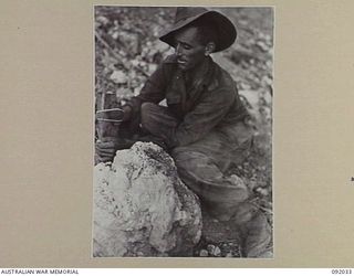 WIRUI MISSION, WEWAK AREA, NEW GUINEA, 1945-05-15. CORPORAL W.G. WEAVE, 2/4 INFANTRY BATTALION, SETTING A GRENADE BOOBY TRAP TO ILLUSTRATE ONE OF THE DEFENCE MEASURES USED BY THE JAPANESE IN THEIR ..