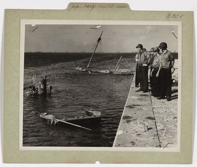 Photograph of Coast Guardsmen Looking Over a Wrecked Japanese Landing Barge