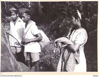 RATONGOR, NEW BRITAIN. 1945-09-13. TWO JAVANESE SAILORS AND A GIRL WALKING ON THE ROAD NEAR THE CHINESE INTERNMENT CAMP. REPRESENTATIVES OF THE AUSTRALIAN RED CROSS CONTACTED THE CAMP FOLLOWING THE ..