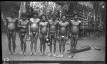 Trobriand men outside yam house; man in center is holding a large gourd, probably for water