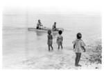 Small outrigger canoe with anthropologists? aboard, children on beach