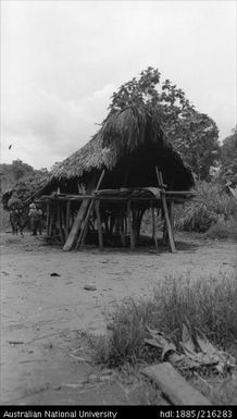 Hut on stilts with four men in background, two of the men in European dress