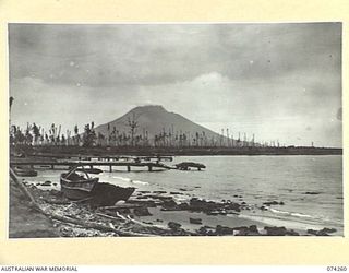 HANSA BAY, NEW GUINEA. 1944-06-22. A GENERAL VIEW OF THE WATERFRONT IN THE 5TH DIVISION SALVAGE GROUP AREA SHOWING THE BOMB BLASTED JETTY AND BARGES ALONG THE SHORE WITH THE VOLCANIC MANAM ISLAND ..