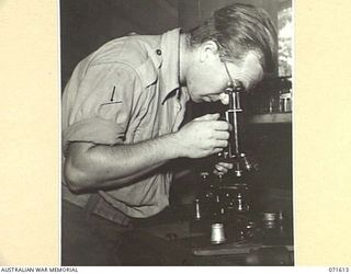 LAE, NEW GUINEA. 1944-03-24. V197944 CRAFTSMAN L. MAXFIELD REPAIRING A HOSPITAL MICROSCOPE IN THE INSTRUMENT REPAIR SHOP AT THE AUSTRALIAN FORTRESS WORKSHOP