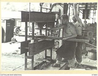 LAE, NEW GUINEA. 1944-06-09. WX15197 CORPORAL S.C. JONES (1), AND QX51604 CRAFTSMAN J.D. WISEMAN (2), MEMBERS OF THE 2/7TH ADVANCED WORKSHOP USE AN APAC HYDRAULIC PRESS TO STRAIGHTEN A BUMPER BAR ..