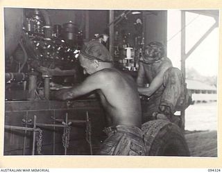 TOROKINA, BOUGAINVILLE. 1945-07-25. PRIVATE J. MOODY (1) AND SERGEANT JAMIESON (2), MEMBERS OF 16 ADVANCED ORDNANCE DEPOT WORKING ON THE MAINTENANCE OF A SEARCHLIGHT GENERATOR