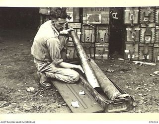 PORT MORESBY, NEW GUINEA. 1944-02-02. VX112502 STAFF SERGEANT H.L. GAYER OF THE 8TH ADVANCED AMMUNITION DEPOT, INSPECTING REPAIRED 3.7 INCH ANTI-AIRCRAFT HIGH EXPLOSIVE SHELLS