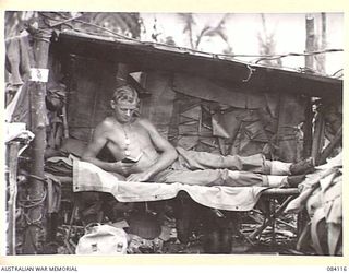 SWAN BEACH, JACQUINOT BAY. NEW BRITAIN. 1944-12-10. PRIVATE H. ALEXANDER, 16 INFANTRY BATTALION, 13 INFANTRY BRIGADE, IN A HUT CONSTRUCTED FROM BANANA LEAVES AND COCONUT FRONDS WITHIN THE ..