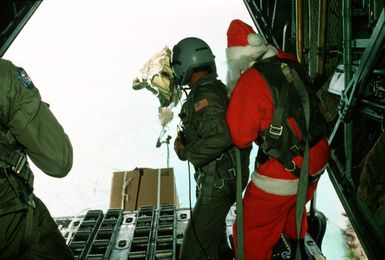 Santa Clause (CPT Mike D'Albertis, 605th Military Airlift Support Squadron) and SSGT Tony Thompson, loadmaster with the 21st Tactical Airlift Squadron, watch as a Christmas Drop container is parachuted toward its destination. The annual airdrop is a humanitarian airdrop effort providing aid to needy islanders throughout Micronesia during the holiday season