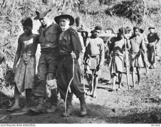 UBERI, NEW GUINEA. 1943-12-19. MEN OF THE 2/9TH AUSTRALIAN INFANTRY BATTALION AND NATIVE CARRIERS ACTING AS EXTRAS DURING THE FILMING OF "RATS OF TOBRUK" BY CHAUVEL'S PRODUCTIONS