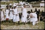 Dancers in white dresses with red trim, with musicians in background