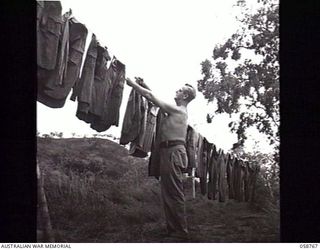 POMPOM VALLEY, NEW GUINEA. 1943-10-26. MUSICIAN NX36087 PRIVATE E. A. COUCHMAN OF THE 7TH AUSTRALIAN DIVISION CONCERT PARTY HANGING THE WASHING ON THE LINE