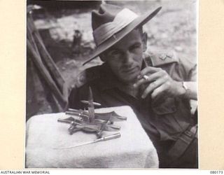 FINSCHHAFEN, NEW GUINEA. 194-07-02. QX10072 LIEUTENANT A.A. NOLAN, 101ST BRIGADE SUPPORT COMPANY, DISPLAYS A LETTER RACK AND OPENER CONSTRUCTED FROM JAPANESE BULLETS AND SHELL CASE. THE INGENUITY ..