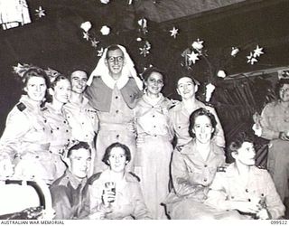 RABAUL, NEW BRITAIN, 1945-12-20. CAPTAIN V. H. HEGARTY, DRESSED IN THE UNIFORM OF A NURSING SISTER, PLAYED THE PART OF SANTA CLAUS AND DISTRIBUTED GIFTS OFF THE CHRISTMAS TREE TO PATIENTS OF WARD ..