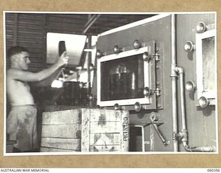 17 MILE, LALOKI RIVER, NEW GUINEA. 1943-11-22. S60128 PRIVATE G. SCHMIDT CHECKING BOTTLES FOR CLEANLINESS, AS THEY ARE REMOVED FROM THE BOTTLE WASHING MACHINE AT THE CORDIAL FACTORY ESTABLISHED AND ..