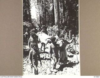 1943-08-19. NEW GUINEA. MOUNT TAMBU. PTE. KEITH WELLS, A.I.F. OF BRISBANE, WOUNDED IN ACTION ON THE KOMIATUM AREA, BEING CARRIED BY NATIVES THROUGH SLUSH AND MUD TO HOSPITAL. WELLS WAS CARRIED FOR ..