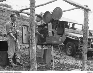 LAKONA, NEW GUINEA. 1944-04-05. PERSONNEL FROM THE ARMY AMENITIES SERVICE PREPARING A 35MM CINE PROJECTOR FOR THE SCREENING OF A FILM AT HEADQUARTERS 8TH INFANTRY BRIGADE USING POWER CARRIED BY THE ..