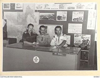 PIVA AIRSTRIP, JACQUINOT BAY, NEW BRITAIN, 1945-07-17. AUSTRALIAN ARMY AND RNZAF OFFICERS CONFERRING IN THE INTELLIGENCE ROOM. IDENTIFIED PERSONNEL ARE:- LT B.A. SYMONDS (1); CAPT I.H. BARNES G3 ..