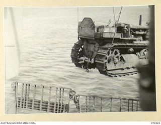 HOSKINS, NEW BRITAIN. 1944-10-08. A TRACTOR OF THE ROYAL AUSTRALIAN ENGINEERS BEING SWUNG ASHORE BY ONE OF THE CRANES OF THE DUTCH TROOPSHIP "SWARTENHONDT" BY A MEMBER OF THE 2/31ST DOCKS OPERATING ..