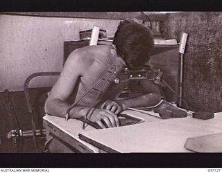 SEVENTEEN MILE, NEW GUINEA. 1943-09-23. VX53224 CORPORAL E. GOODE OF THE 2/1ST AUSTRALIAN ARMY TOPOGRAPHICAL SURVEY COMPANY, EXAMINING AERIAL PHOTOGRAPHS UNDER A STEREOSCOPE