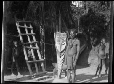 Man standing beside a  house ladder and a carved piece of timber, Tambunum, Sepik River, New Guinea, 1935, 2 / Sarah Chinnery