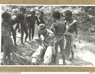 PA PA, PAPUA. 1943-12-02. VX80954 CAPTAIN A. G. SCHOLES, INTELLIGENCE OFFICER, HEADQUARTERS, NEW GUINEA FORCE LIGHTS AN AFTER LUNCH PIPE SURROUNDED BY NATIVE CHILDREN