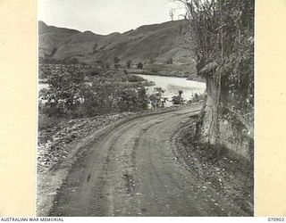 WAU - LAE ROAD, NEW GUINEA, 1944-02-26. THE 1ST MECHANICAL EQUIPMENT PLATOON 2/1ST RAILWAY CONSTRUCTION COMPANY (MECHANICAL EQUIPMENT), ROYAL AUSTRALIAN ENGINEERS CAMP PICTURED BEYOND THE WATUT ..