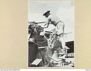 PORT MORESBY, PAPUA. 1942-07. AN A.I.F. "ACK ACK" GUNNER APPLYING GREASE TO THE BREECH MECHANISM OF AN ANTI AIRCRAFT GUN AFTER AN ENGAGEMENT WITH JAPANESE PLANES IN NEW GUINEA