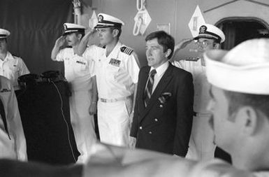 Secretary of the Navy John F. Lehman Jr., center, stands as officers and crewmen salute the colors during his visit aboard the aircraft carrier USS KITTY HAWK (CV-63)