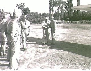 THE SOLOMON ISLANDS, 1945. AN US OFFICER FAREWELLS AMERICAN MAJOR GENERAL R.J. MITCHELL ON HIS DEPARTURE FROM BOUGAINVILLE ISLAND. PART OF THE GENERAL'S FAREWELL PARADE AND A CORSAIR AIRCRAFT CAN ..